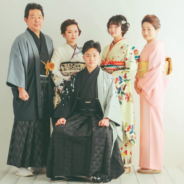 alt=成人式の前撮り時における家族記念撮影の様子。紋付袴を凛々しく着こなした主役の男性を中心に、色鮮やかな振袖や上品な訪問着、着物姿の父親など、家族全員が美しい和装に身を包んでスタジオに並ぶ、一生の記念となる華やかな家族写真
