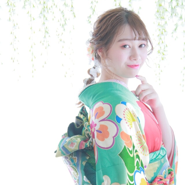 alt=鮮やかなグリーンの振袖に身を包んだ新成人の前撮り記念撮影。大きな花柄が施された着物に華やかな帯結び、トレンドのヘアアレンジと髪飾りがマッチしたコーディネート。スタジオの白い背景と自然光が、二十歳の晴れ姿を美しく引き立てる様子